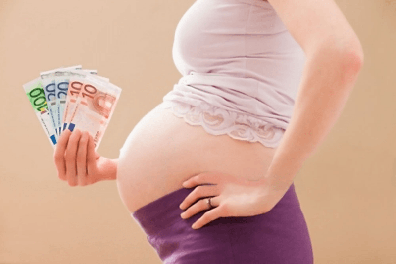 Bonus mamme, una donna incinta di profilo con delle banconote in mano